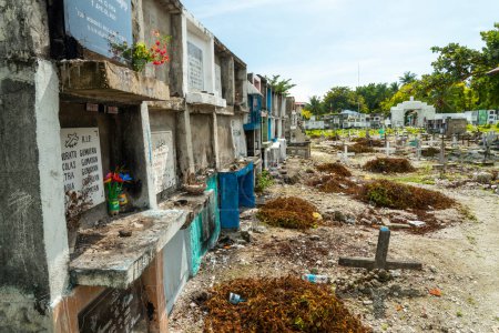 Foto de Atmosférico cementerio católico filipino, junto al mar del estrecho de Cebú, muchas tumbas con cámara, que alberga a los fallecidos, cientos de crucifijos, marcando tumbas, dispuestos al azar, por el muro del mar y la playa. - Imagen libre de derechos