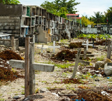 Foto de Atmosférico cementerio católico filipino, junto al mar del estrecho de Cebú, muchas tumbas con cámara, cientos de crucifijos, cubiertos por escombros de tormenta, tumbas de lugareños, colocadas al azar, junto al muro del mar. - Imagen libre de derechos