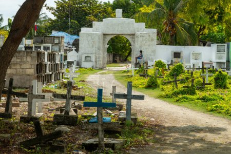Foto de Atmosférico cementerio católico filipino, junto al mar del estrecho de Cebú, tumbas de la población local fallecida, dispuestos al azar y parcialmente sombreados por un árbol del sol de hornear. - Imagen libre de derechos