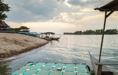 Foto de Al atardecer, en el río Mekong, pequeños barcos de madera que transportan a los viajeros hacia y desde las islas Nakasong y Don Som, en el punto del muelle de la playa de arena, puerta principal de entrada a la isla Don Det. - Imagen libre de derechos