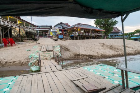 Foto de Al atardecer, en el río Mekong, pequeños barcos de madera transportan a los viajeros hacia y desde las islas Nakasong y Don Som, aquí en el muelle flotante de la playa de arena, puerta principal a la isla Don Det. - Imagen libre de derechos