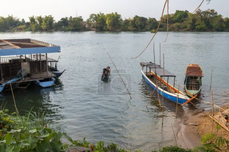 Foto de Pequeña plataforma de ferry flotante, en el río Mekong, pequeños barcos de madera transportan personas hacia y desde las islas Nakasong y Don Som, en el punto del muelle de la playa de arena, ruta principal hacia la isla Don Det. - Imagen libre de derechos