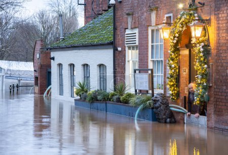 Téléchargez les photos : Worcester, Worcestershire, Royaume-Uni-03 janvier 2024 : Les eaux d'inondation, causées par les récentes pluies hivernales, les tempêtes et les hauts niveaux de la rivière, entrent dans un pub au bord de la rivière, alors que des efforts sont déployés pour l'évacuer par des pompes à eau. - en image libre de droit