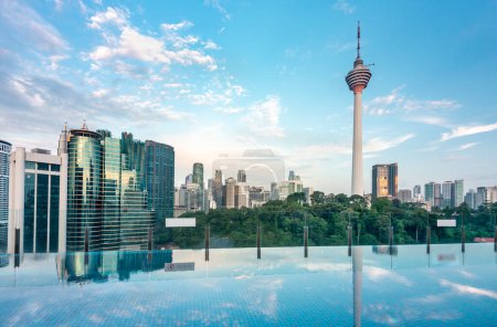 Atemberaubender Blick auf die Stadt KL und Menara Kuala Lumpur, bei Sonnenuntergang mit blauem Infinity-Pool auf der Dachterrasse und blauem Himmel mit Wolken, Wolkenkratzern und Bäumen im KLCC-Park.