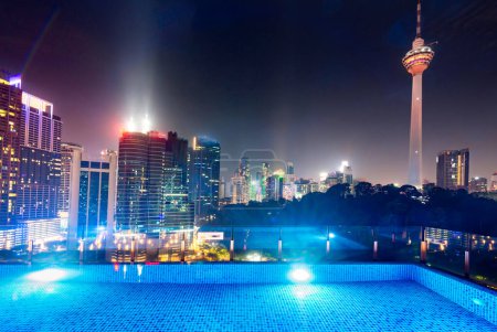 Atemberaubender Rootop-Nachtblick auf die Wolkenkratzer der Stadt KL, nachts hell erleuchtet, eleganter Pool im Vordergrund mit atemberaubendem, hochaufragendem Panoramablick auf die moderne Skyline der Stadt.