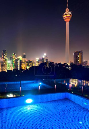 Atemberaubender Rootop-Nachtblick auf die Wolkenkratzer der Stadt KL, nachts hell erleuchtet, eleganter Pool im Vordergrund mit atemberaubendem, hochaufragendem Panoramablick auf die moderne Skyline der Stadt.