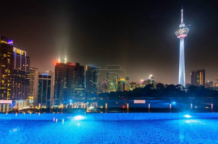 Stunning rootop nighttime view of KL city skyscrapers,brightly lit up at night, sleek pool in the foreground with stunning,high angle panoramic views of the modern city skyline.