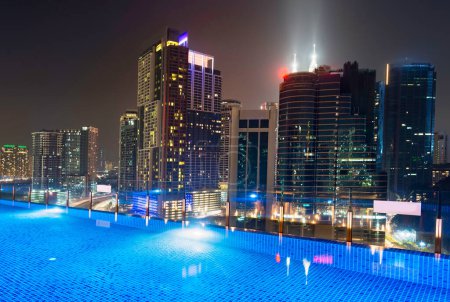 Impresionante vista nocturna de la azotea de los rascacielos de la ciudad de KL, brillantemente iluminada por la noche, piscina elegante en primer plano con impresionantes vistas panorámicas de alto ángulo del horizonte moderno de la ciudad.
