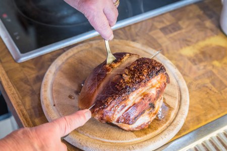 Real hearty homemade roast pork is cut into portions on a wooden board in the kitchen, Germany