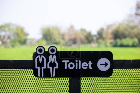 Selective focus women's and men's restroom signs on a green rice field background.