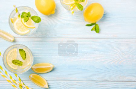 Foto de Refrescante bebida fría de verano con limón y menta sobre fondo de madera azul claro, vista superior, disposición plana, espacio para copiar
. - Imagen libre de derechos