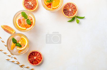 Téléchargez les photos : Cold refreshing drink with blood orange slices in a glass on a concrete background. Top view, flat lay, copy space. - en image libre de droit