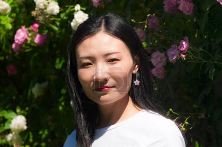 Photo for An attractive happy chinese woman standing in elizabeth park's rose garden on a sunny day. - Royalty Free Image