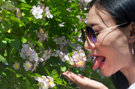 Photo for A chinese woman with her tongue out looking like she will eat roses at a garden in west hartford connecticut. - Royalty Free Image