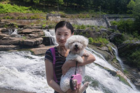 Foto de Una mujer china sosteniendo un bichon frise en Great Falls en Falls Village Canaan Connecticut en un soleado día de verano. - Imagen libre de derechos