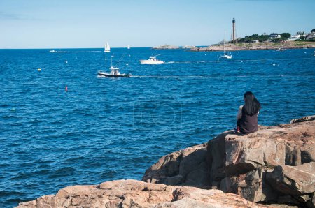 Eine Frau sitzt auf Felsen in Galehead mit Blick auf den Marblehead Harbor in Massachusetts.