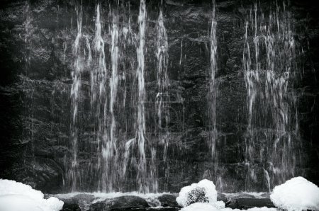 Wasser fließt im Winter in Neuengland schwarz-weiß über eine Mauer.