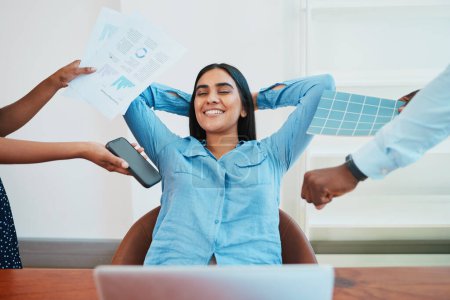 Photo for Young South Asian woman relaxes in office chair while coworkers make demands. High quality photo - Royalty Free Image