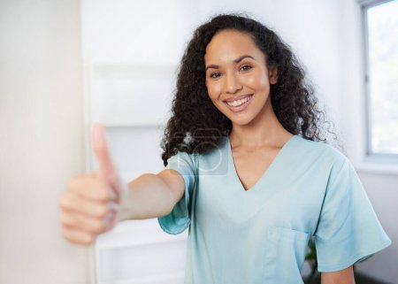 Beautiful young healthcare professional gives thumbs up wearing scrubs. High quality photo