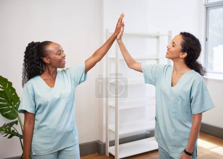 Two female doctors high five in clinic, wearing scrubs celebrate success. High quality photo