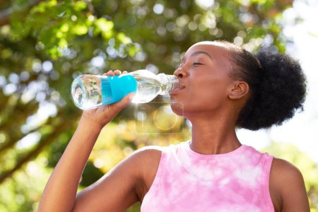 Foto de Primer plano de la joven mujer negra bebiendo agua de la botella de vidrio en el parque, diversión yoga. Foto de alta calidad - Imagen libre de derechos