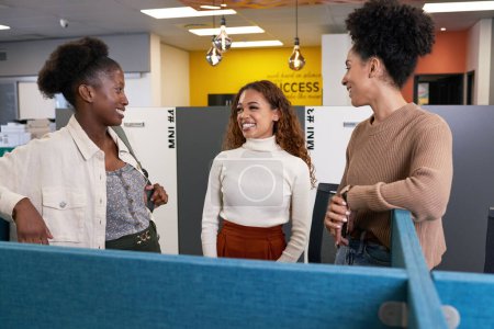 Photo for Three young diverse female colleagues stand and chat in open plan office. High quality photo - Royalty Free Image