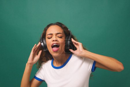 Junge Frau tanzt mit Kopfhörern, grüner Studiohintergrund. Hochwertiges Foto