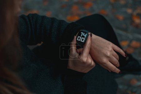 Photo for A woman looking at her smartwatch on hand. Time on the clock 14-00.Close up view with blurred background. Full frame. - Royalty Free Image