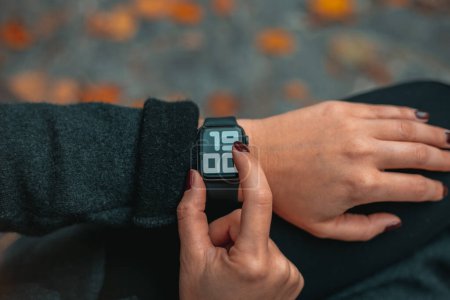 Photo for Photo of woman hands touching setting of digital smart watch in park. The time on the clock is 19-00. - Royalty Free Image