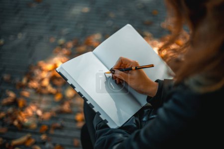 Photo for Woman with notepad. Close-up of a young girl writing into her diary, in the park. A woman writes in a notebook with a pen on the street. Web banner. Full Frame. High quality photo - Royalty Free Image