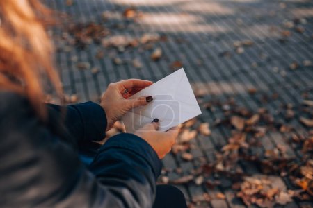 Téléchargez les photos : Femme ouvre une enveloppe blanche avec une lettre. Feuillage d'automne dans le fond. Photo de haute qualité - en image libre de droit