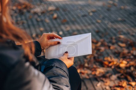 Woman opens a white envelope with a letter. Autumn foliage in the background.High quality photo