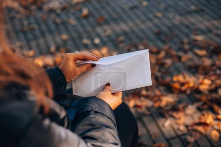 Frau öffnet einen weißen Umschlag mit einem Brief. Herbstliches Laub im Hintergrund. Hochwertiges Foto