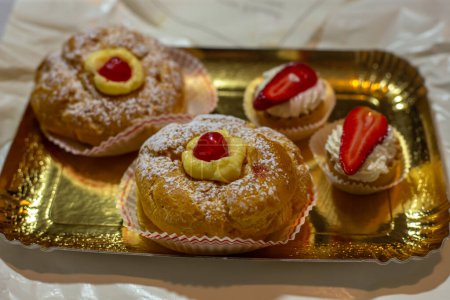 Italian dessert Zeppole di San Giuseppe, zeppola baked puffs made from choux pastry, filled and decorated with custard cream and cherry. Close-up.