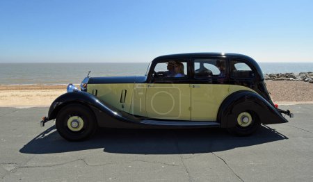 Photo for FELIXSTOWE, SUFFOLK, ENGLAND - MAY 06, 2018:  Vintage  Rolls Royce Motor Car being driven on seafront promenade beach and sea in background - Royalty Free Image
