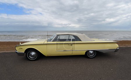 Photo for FELIXSTOWE, SUFFOLK, ENGLAND - MAY 05, 2019: Classic Yellow Ford Galaxie Sunliner motor car parked on seafront promenade beach and sea in background. - Royalty Free Image