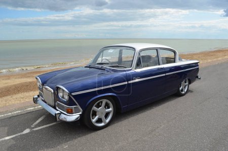 Photo for FELIXSTOWE, SUFFOLK, ENGLAND - AUGUST 23, 2014: Classic Blue and White Humber Sceptre on seafront promenade beach and sea in background - Royalty Free Image