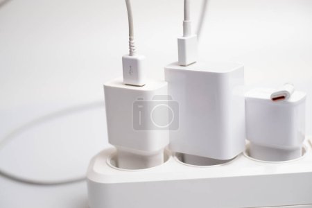 Téléchargez les photos : De nombreux chargeurs sont connectés à une prise électrique sur fond blanc. - en image libre de droit