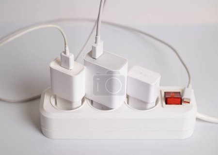 Many chargers are connected to an electrical outlet on a white background.