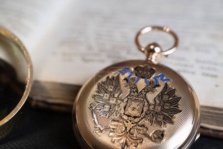 Gold pocket watch "Pavel Bure" on a gold pendant. Royal Russia. pocket watch on a dark background with books. Image of an antique gold pocket watch on an old antique book.