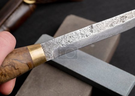 Téléchargez les photos : Aiguiser un couteau japonais avec une pierre à aiguiser. Magnifique motif ondulé de lame en acier Damas. lame en acier au carbone élevé. - en image libre de droit