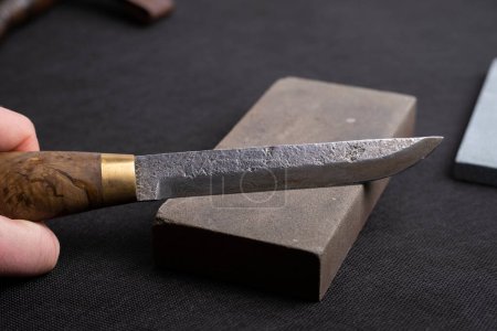 Photo for Sharpening a Japanese knife with a whetstone. Beautiful wavy pattern of Damascus steel blade. high carbon steel blade. - Royalty Free Image