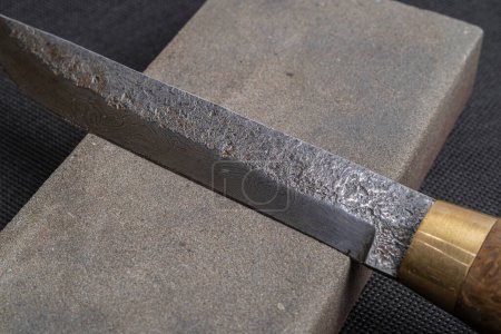 Photo for Sharpening a Japanese knife with a whetstone. Beautiful wavy pattern of Damascus steel blade. high carbon steel blade. - Royalty Free Image