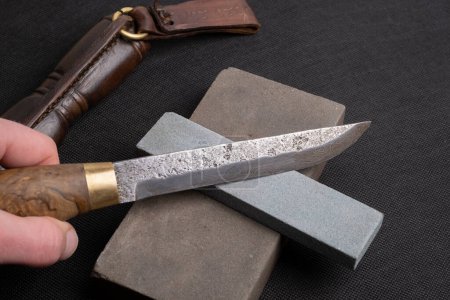 Téléchargez les photos : Aiguiser un couteau japonais avec une pierre à aiguiser. Magnifique motif ondulé de lame en acier Damas. lame en acier au carbone élevé. - en image libre de droit