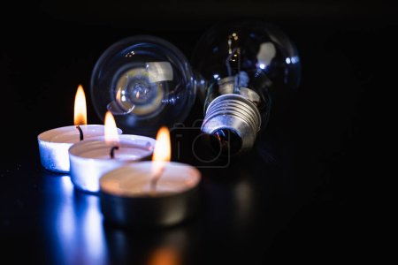 Elektrische Lampe und Kerze auf dunklem Hintergrund. Glühlampe und Kerze. Nein oder Stromausfall. Hohe Strompreise. Strom sparen.