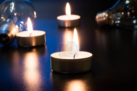 Elektrische Lampe und Kerze auf dunklem Hintergrund. Glühlampe und Kerze. Nein oder Stromausfall. Hohe Strompreise. Strom sparen.