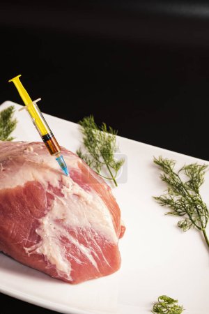 Foto de Inyección de una jeringa en carne cruda sobre un fondo oscuro.Ilustración conceptual de hormonas y antibióticos en la producción de alimentos. - Imagen libre de derechos