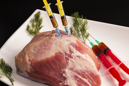 Foto de Inyección de una jeringa en carne cruda sobre un fondo oscuro.Ilustración conceptual de hormonas y antibióticos en la producción de alimentos. - Imagen libre de derechos