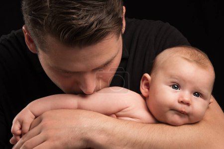 Foto de Un padre joven besa suavemente a un bebé recién nacido. La ternura y el amor de un padre. - Imagen libre de derechos