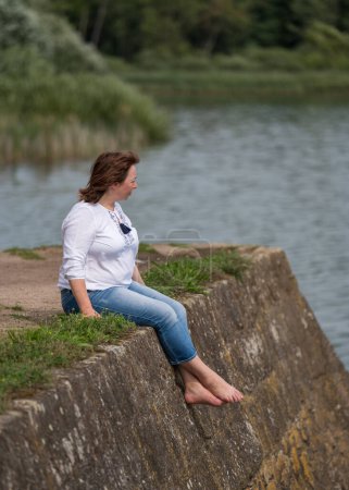 Eine Frau mittleren Alters genießt die schöne Landschaft. Sitzt am Rand der Seebrücke mit Blick auf den See. 